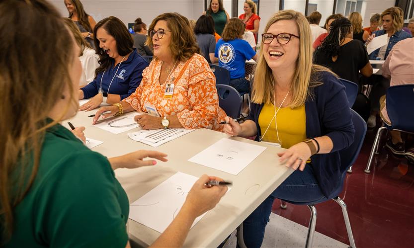 A woman laughs as she draws the person sitting across from her